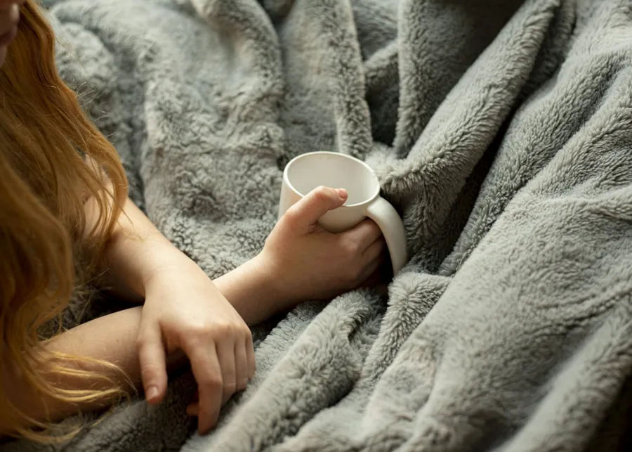 Femme blottie dans un plaid, une tasse chaude entre les mains